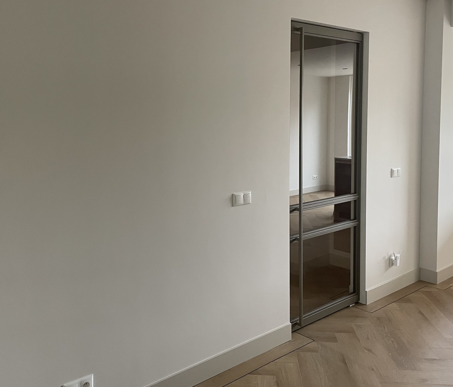 Gladde witte gestucte wand met een stalen glazen schuifdeur en visgraatvloer